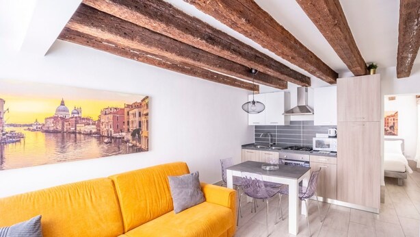 Une cuisine moderne avec un coin repas, un canapé jaune et un tableau représentant un paysage urbain accroché au mur.