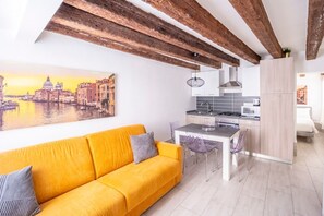 A modern kitchen with a dining area, a yellow sofa, and a cityscape painting on the wall.