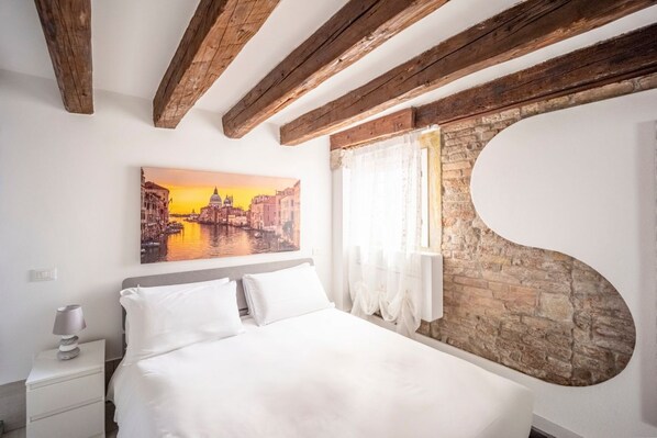 Ein Schlafzimmer mit einem Bett, einem Nachttisch, einem Stadtbildgemälde und freiliegenden Holzbalken.
