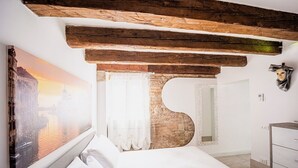 Une chambre avec une grande fenêtre, un lit, une poutre en bois au plafond et un tableau représentant un paysage urbain.