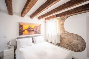 A bedroom with a bed, a nightstand, a painting of a cityscape, and exposed wooden beams.