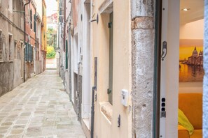 Une ruelle étroite pavée de pierres, avec des bâtiments de chaque côté et une porte donnant sur un panorama urbain.