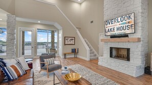 A spacious living room with a stone fireplace, a large window, and a staircase leading to an upper level.