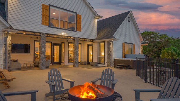 A house with a covered patio area featuring a fire pit, outdoor seating, and stone pillars.