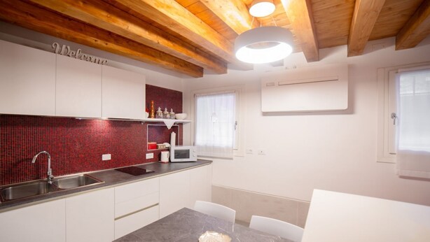 A modern kitchen with white cabinets, a red-tiled backsplash, a microwave, and a sink. - Ca' Gritti, Castello next to Arsenale (Venezia)