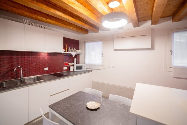 Una cocina moderna con armarios blancos, salpicadero de baldosas rojas, microondas y lavaplatos.