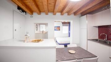A modern kitchen with white cabinets, a marble countertop, and a wooden ceiling.
