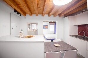 Una cocina moderna con armarios blancos, encimera de mármol y techo de madera.