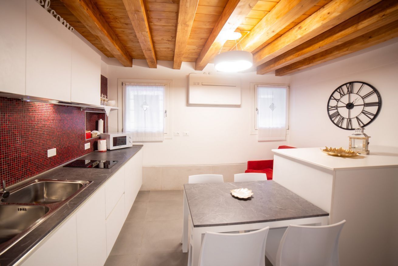 Une cuisine moderne avec des meubles blancs, un dosseret en carreaux rouges, des appareils en acier inoxydable et un plafond en bois.