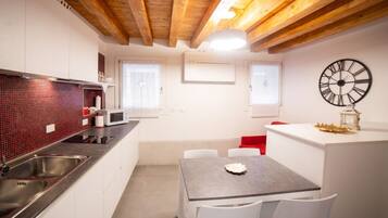 Una cucina moderna con mobili bianchi, una parete di fondo in piastrelle rosse, elettrodomestici in acciaio inossidabile e un soffitto in legno.