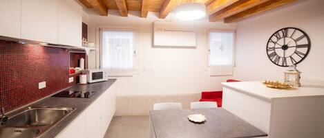 A modern kitchen with white cabinets, a red-tiled backsplash, stainless steel appliances, and a wooden ceiling.