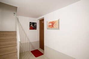 Un couloir avec un escalier en bois, un tapis rouge et deux œuvres d’art encadrées accrochées aux murs.