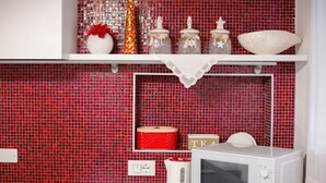 A kitchen with red mosaic tiles, a white microwave, a red kettle, and a shelf with decorative jars and a bowl. - Ca' Gritti, Castello next to Arsenale (Venezia)