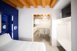 Une chambre avec un lit, une armoire et un téléviseur. Il y a également une petite kitchenette équipée d’une table et de chaises.