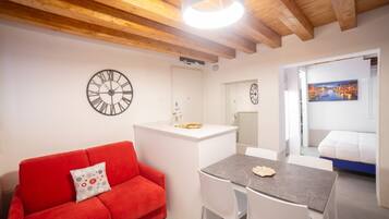 Un ambiente compatto con un divano rosso, un piccolo tavolo da pranzo e un angolo cottura bianco.