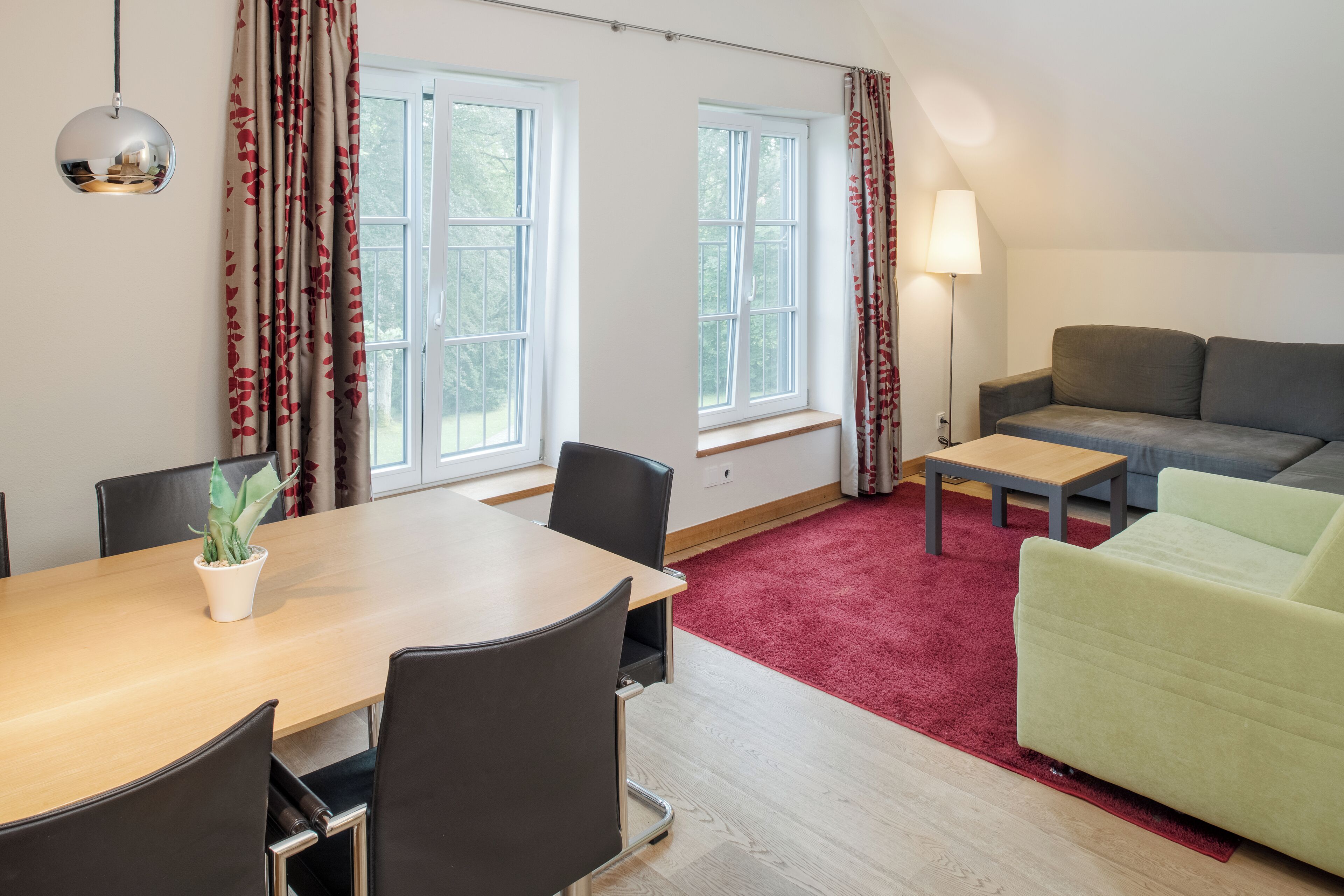 Ein modernes Wohnzimmer mit einem Holzespeisetisch, schwarzen Stühlen, einem grauen Sofa und einem roten Teppich.