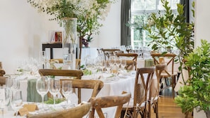Un espace repas avec des chaises et des tables en bois, des nappes blanches et des centres de table floraux.