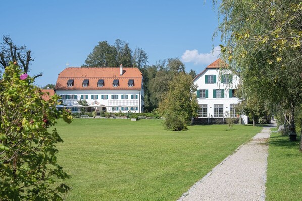 Een groot, wit gebouw met een rood dak en groene luiken, omringd door een verzorgd gazon en een grindpad.