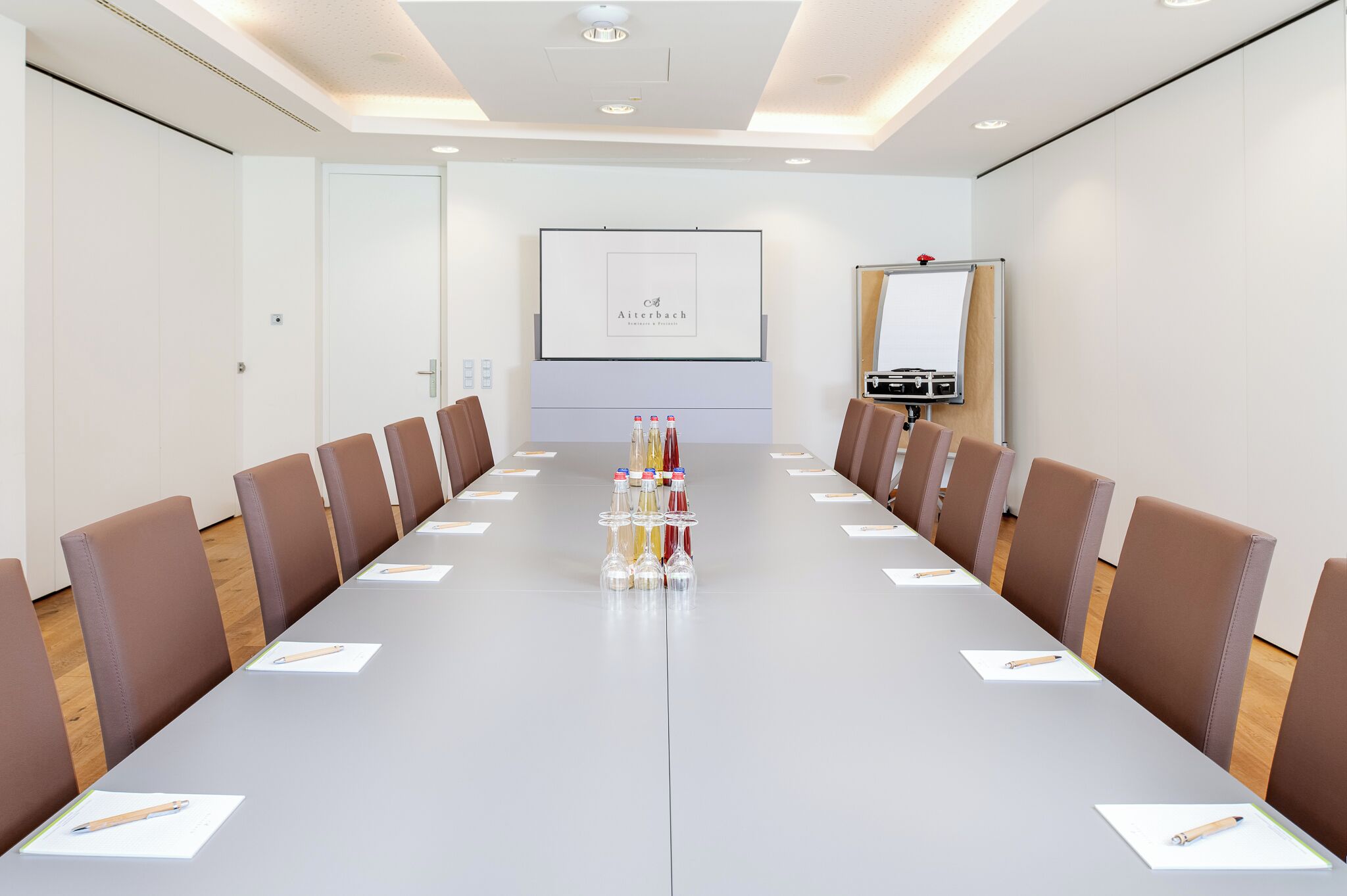 A conference room with a long table, brown chairs, a projector screen, and a whiteboard.