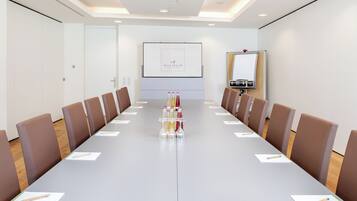 A conference room with a long table, brown chairs, a projector screen, and a whiteboard.
