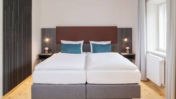 A double bed with a wooden headboard, two bedside tables with lamps, and a view of the outdoors through a window with curtains.