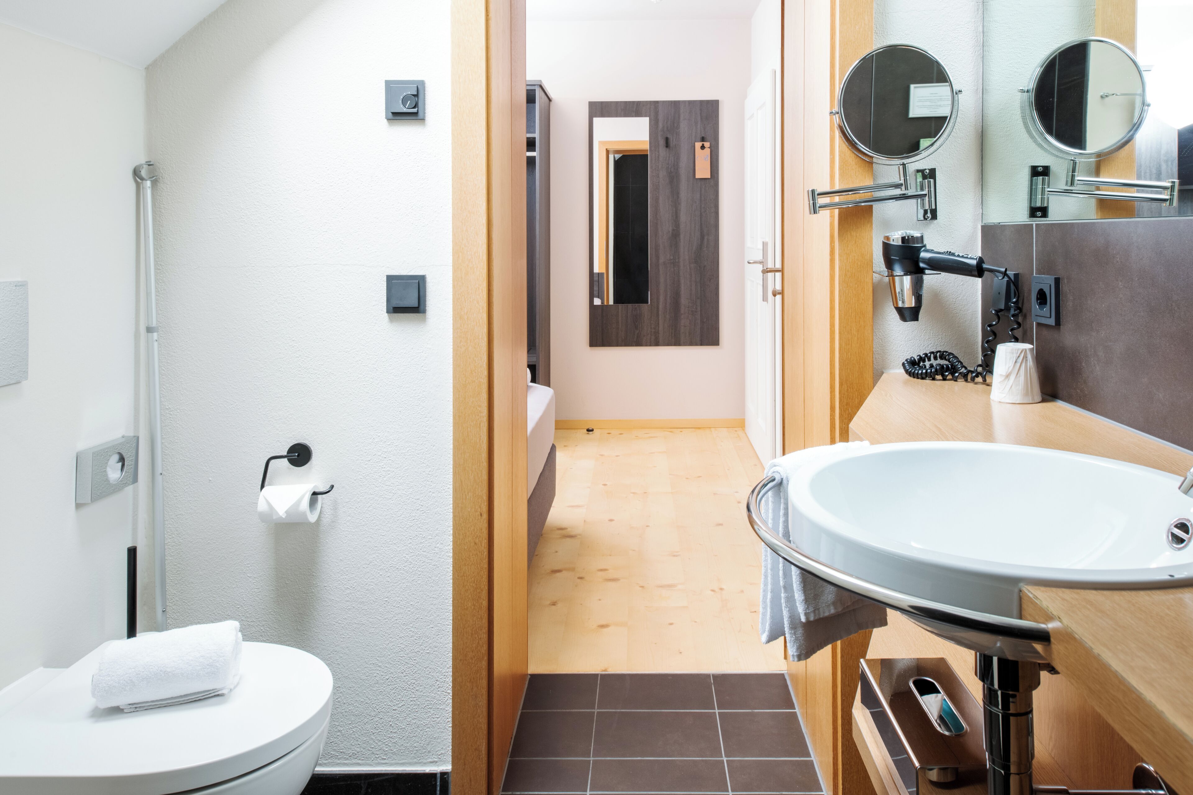 Un baño moderno con inodoro blanco, lavamanos, espejo y toallero.