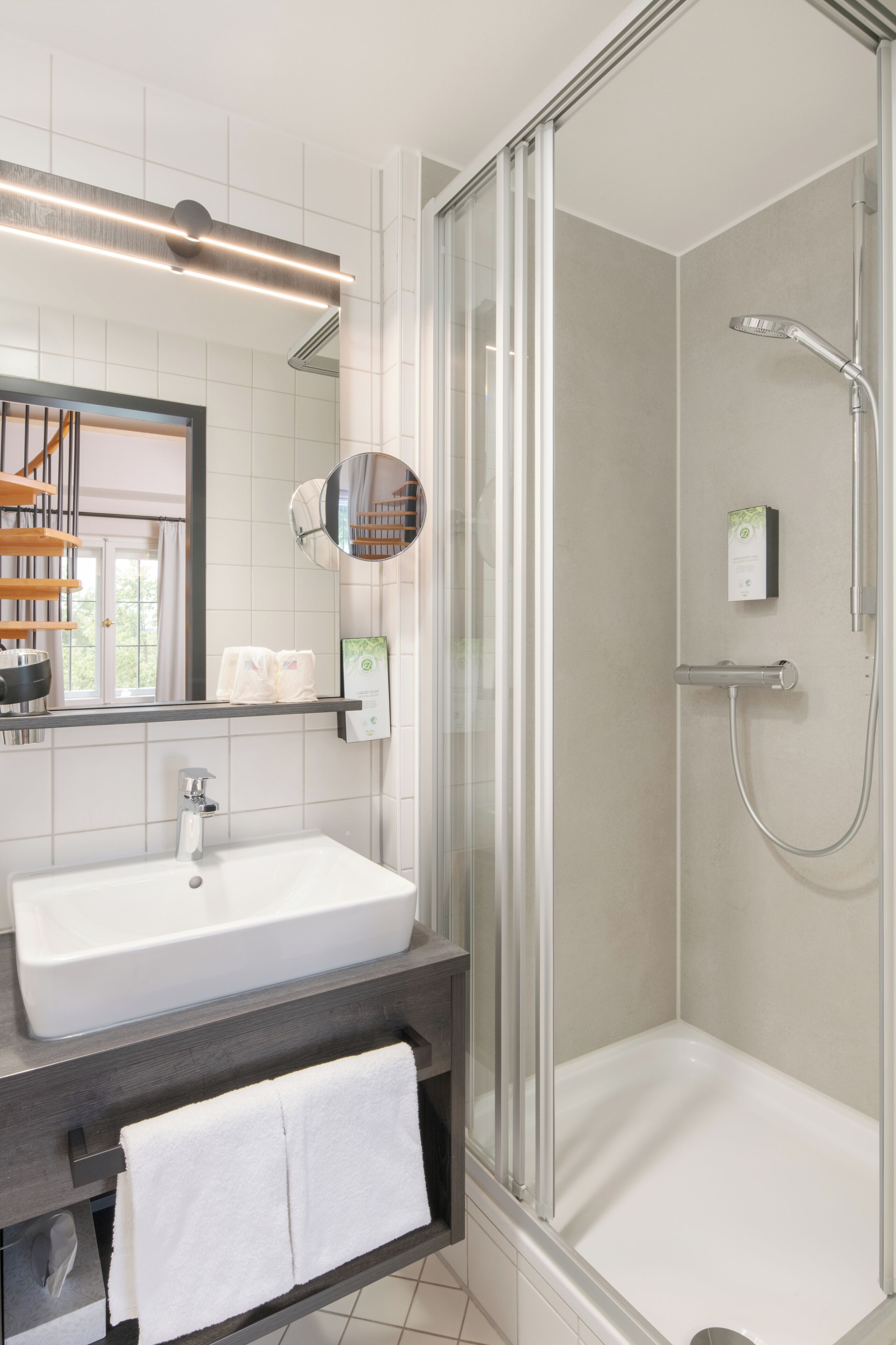 Un baño moderno con ducha envuelta en vidrio, un lavabo blanco y un espejo sobre el mueble.