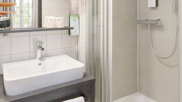 Un baño moderno con ducha envuelta en vidrio, un lavabo blanco y un espejo sobre el mueble.