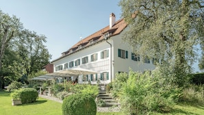 Un grand bâtiment blanc, doté d’un toit recouvert de tuiles, entouré de jardins et d’arbres bien entretenus.