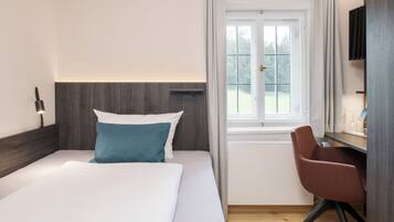 Habitación de hotel con cama, escritorio, silla, ventana y vista a zonas verdes.