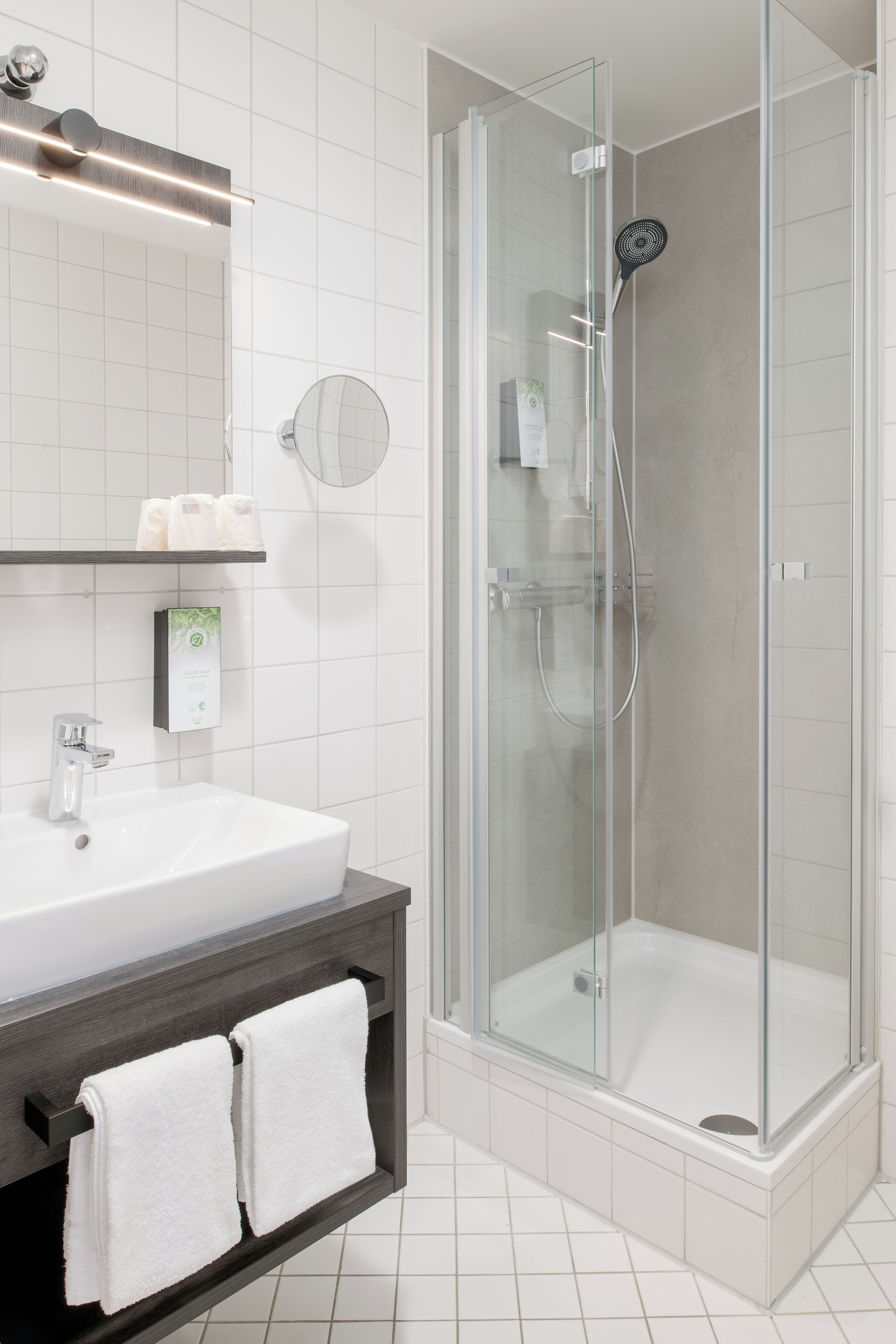 Ein modernes Badezimmer mit einer gläsernen Duschkabine, einem weißen Waschbecken und einem dunklen Holz-Waschtisch.