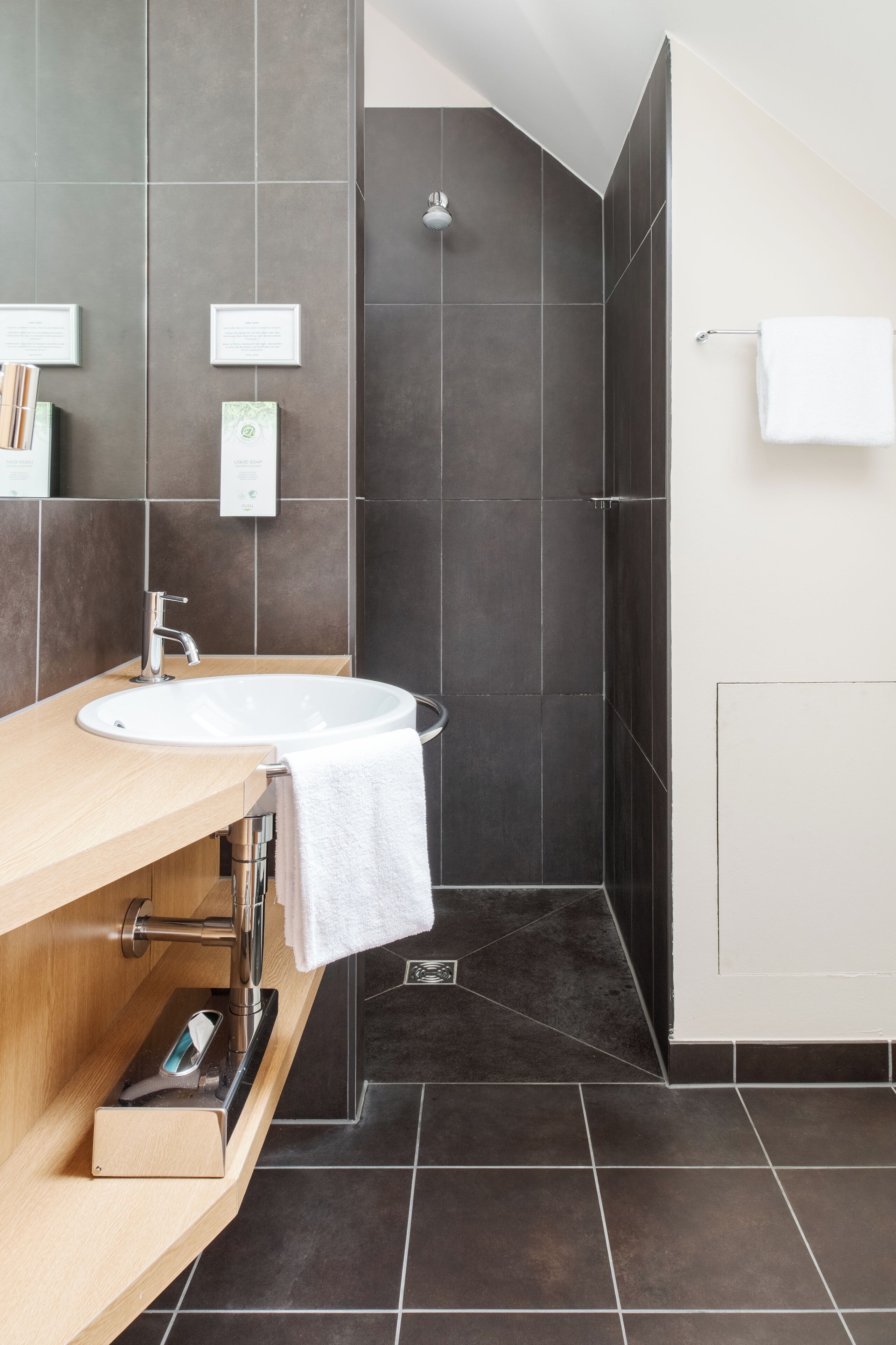 Un baño moderno con un lavabo redondo, ducha y paredes de azulejos oscuros.