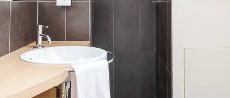 Un baño moderno con un lavabo redondo, ducha y paredes de azulejos oscuros.