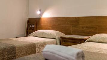 Habitación de hotel con dos camas, cabecero de madera, mesita de noche y lámpara de pared.