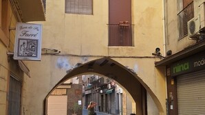 Une rue étroite où l’on aperçoit un piéton, des bâtiments de chaque côté et une enseigne indiquant « Form de Pa Farre ».