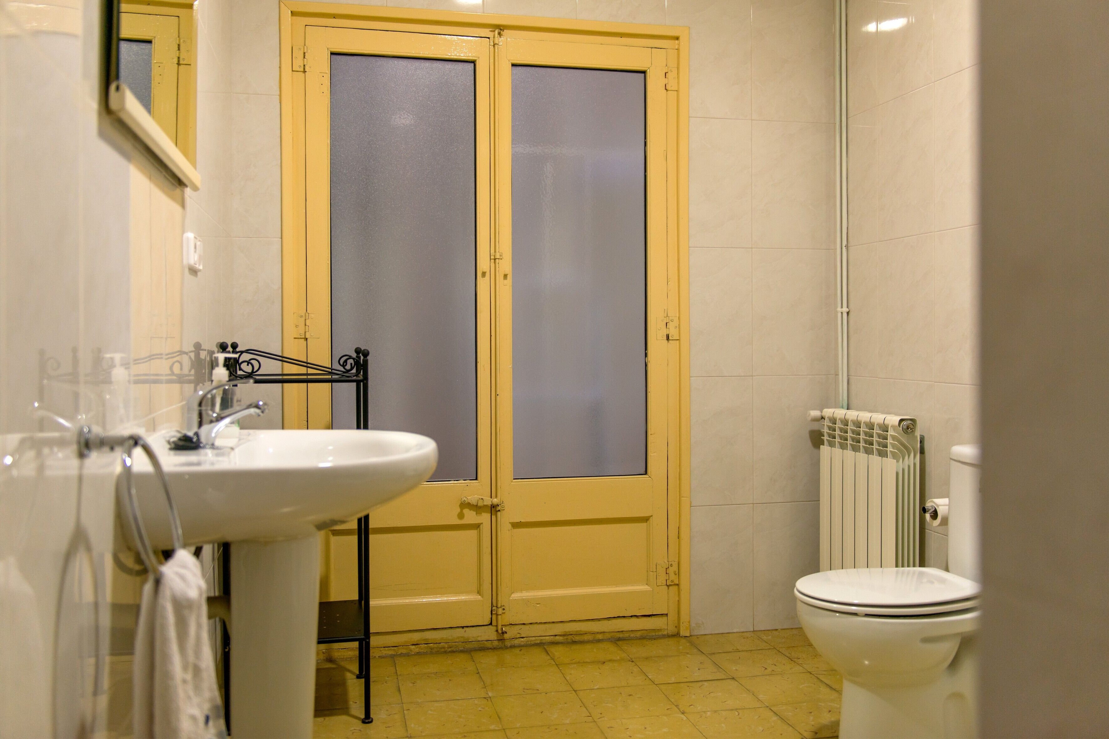 Un baño con un lavamanos blanco, un inodoro y una puerta doble con paneles de vidrio satinado.