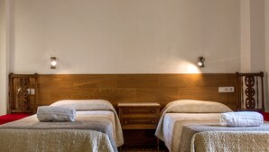Une chambre d’hôtel avec deux lits, une tête de lit en bois, des tables de chevet et des lampes fixées au mur.