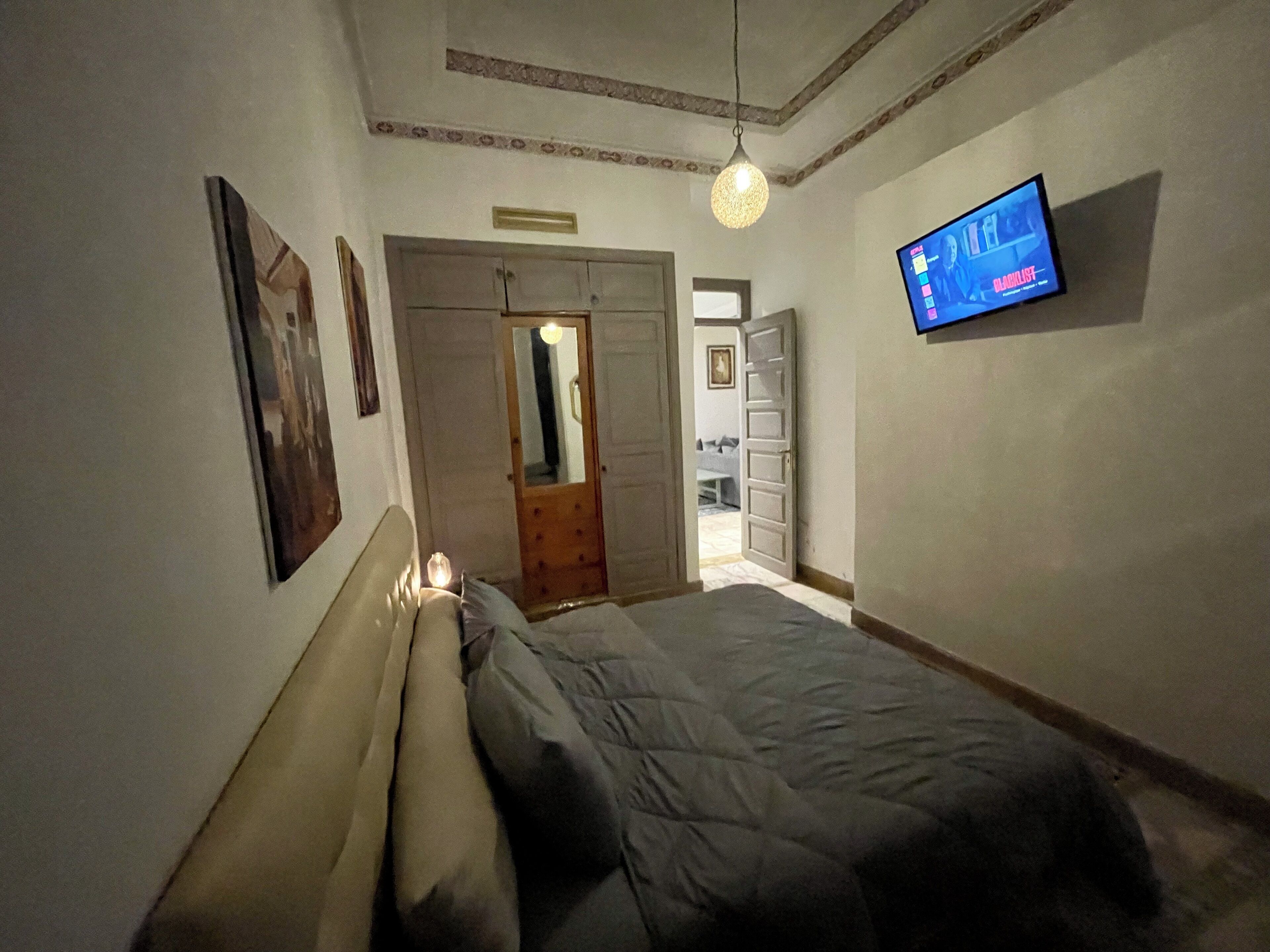 Una camera da letto con un letto, una televisione montata a parete e una porta che dà su un'altra stanza.