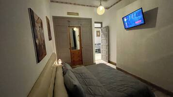 A bedroom with a bed, a television mounted on the wall, and a door leading to another room.