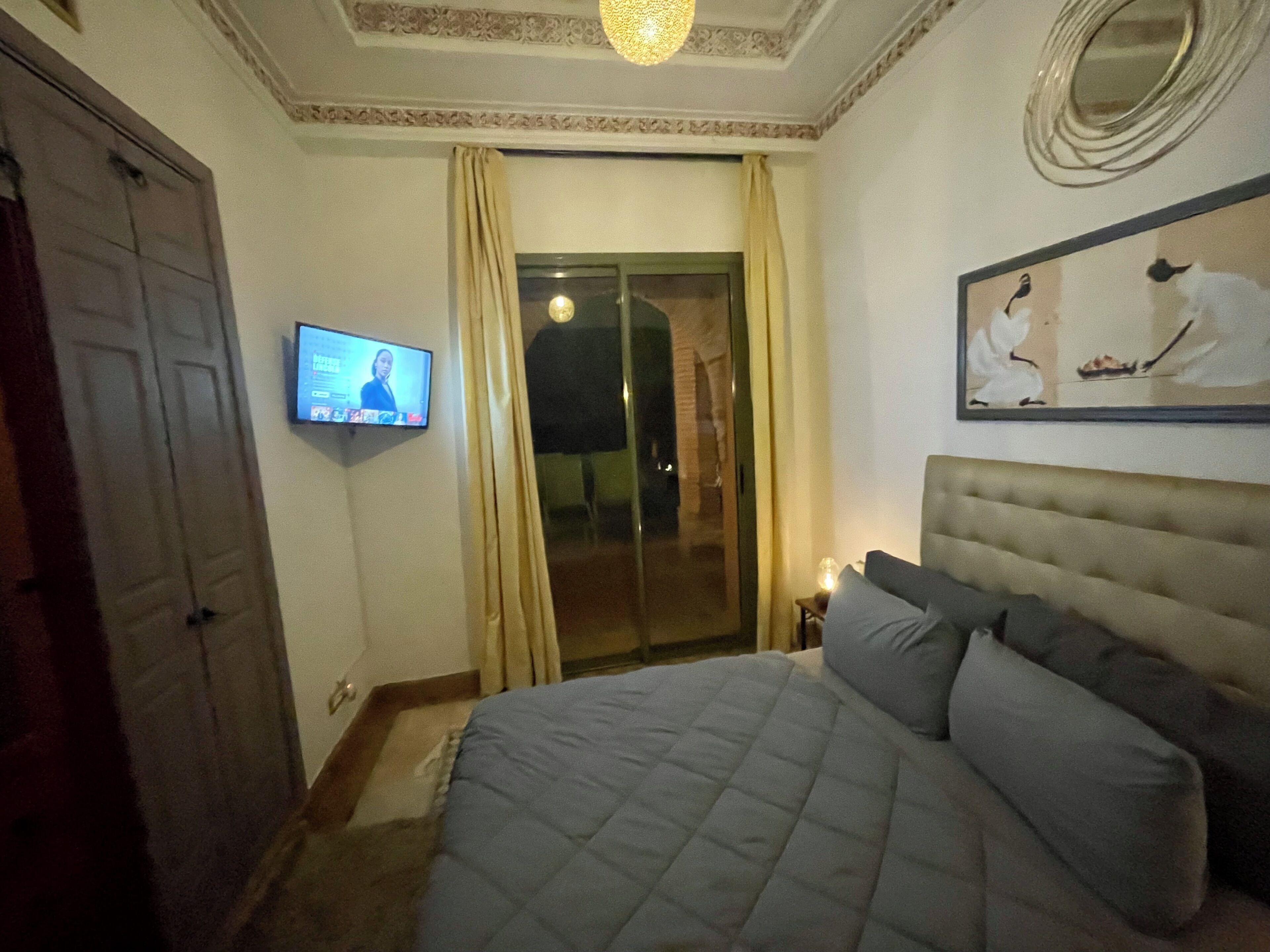 A bedroom with a bed, a television on the wall, a painting, and a door.