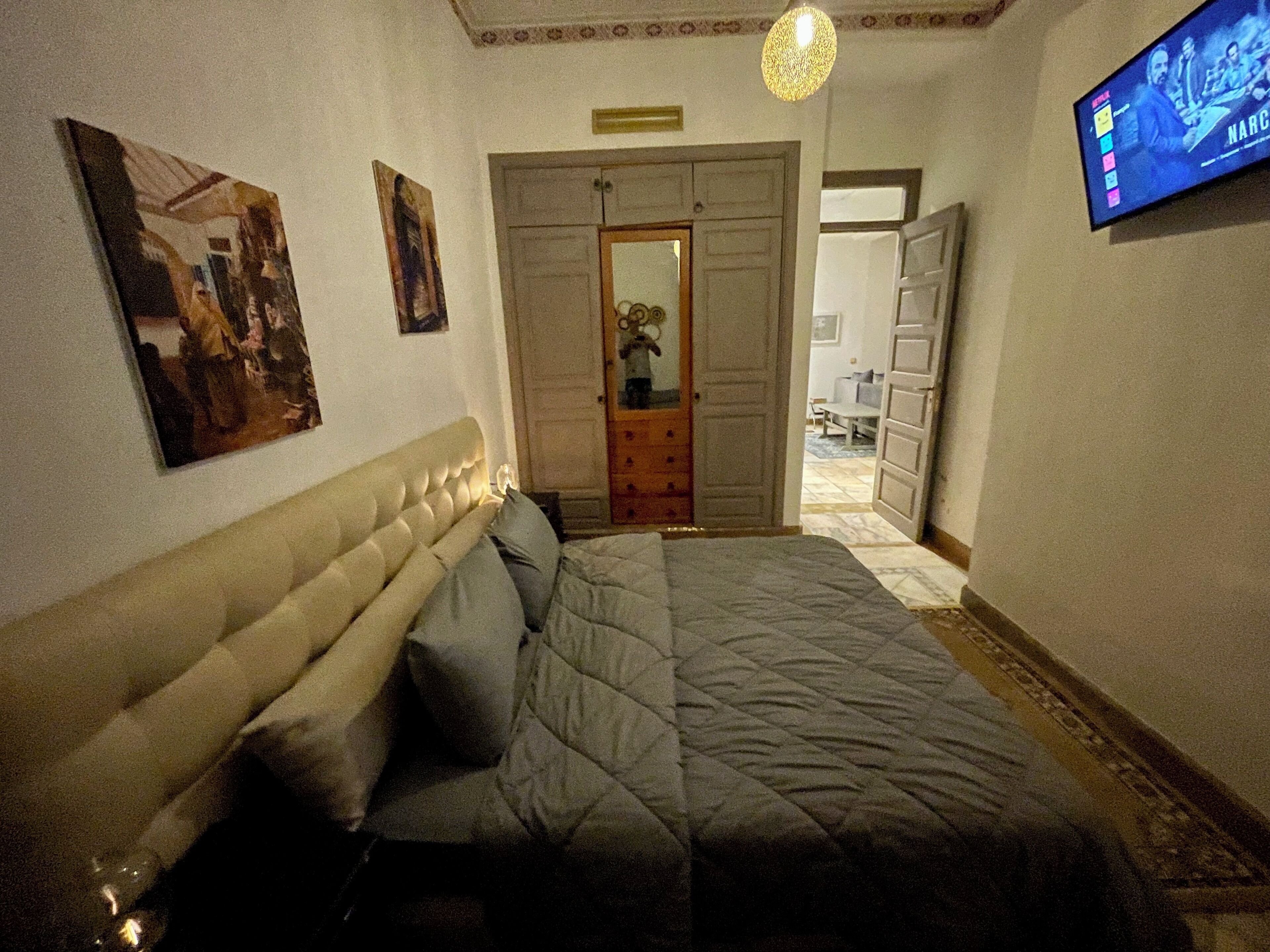 Een slaapkamer met een groot bed, een televisie aan de muur en een deur naar een andere kamer.