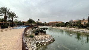 A landscaped area with a curved water feature, a brick pathway, and palm trees. - Au Coeur De La Palmeraie De Marrakech  (Marrakech)