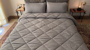 A neatly made bed with a grey quilt, two grey pillows, and a tufted headboard. There are two bedside tables with lamps and a remote control on one. - Au Coeur De La Palmeraie De Marrakech  (Marrakech)