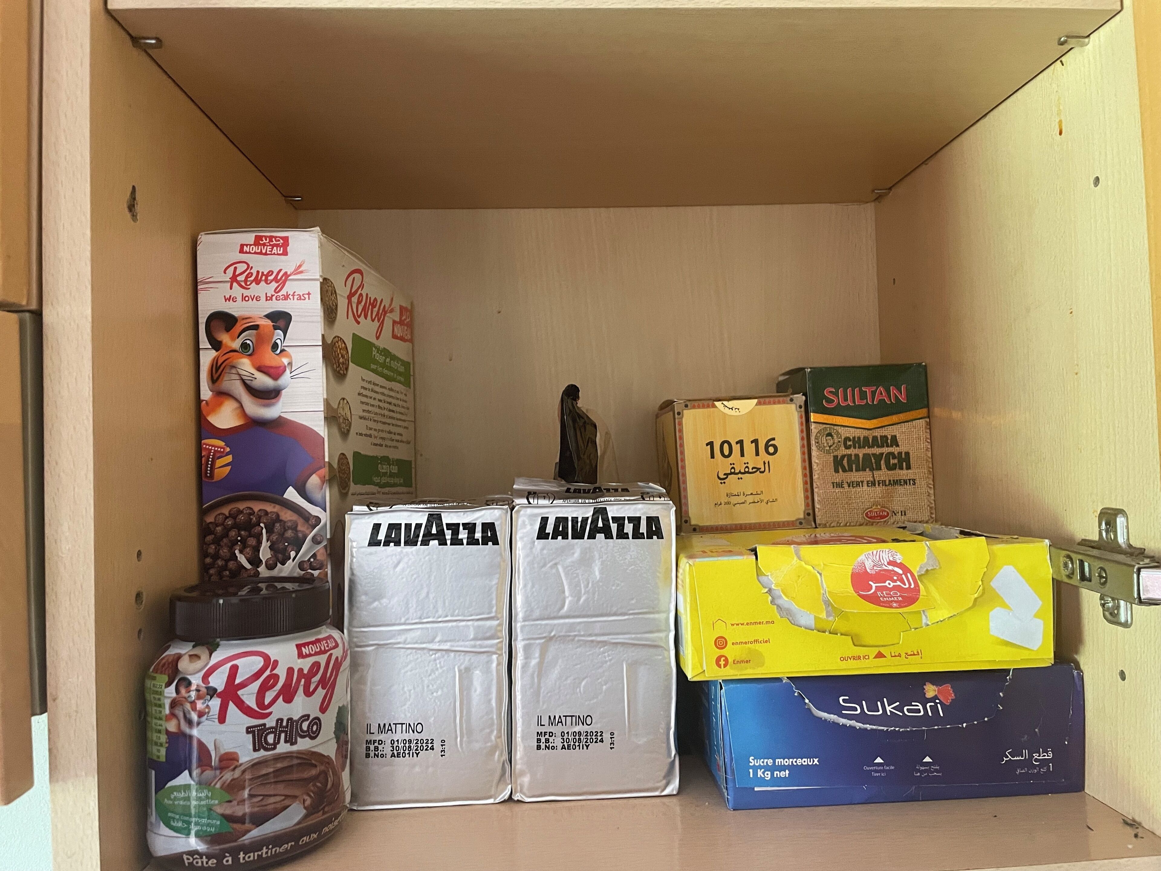 Un área de almacenamiento con diversos productos alimenticios, incluyendo cajas de chocolate Riveya, café Lavazza, dulces Sukari y filamentos Sultana.