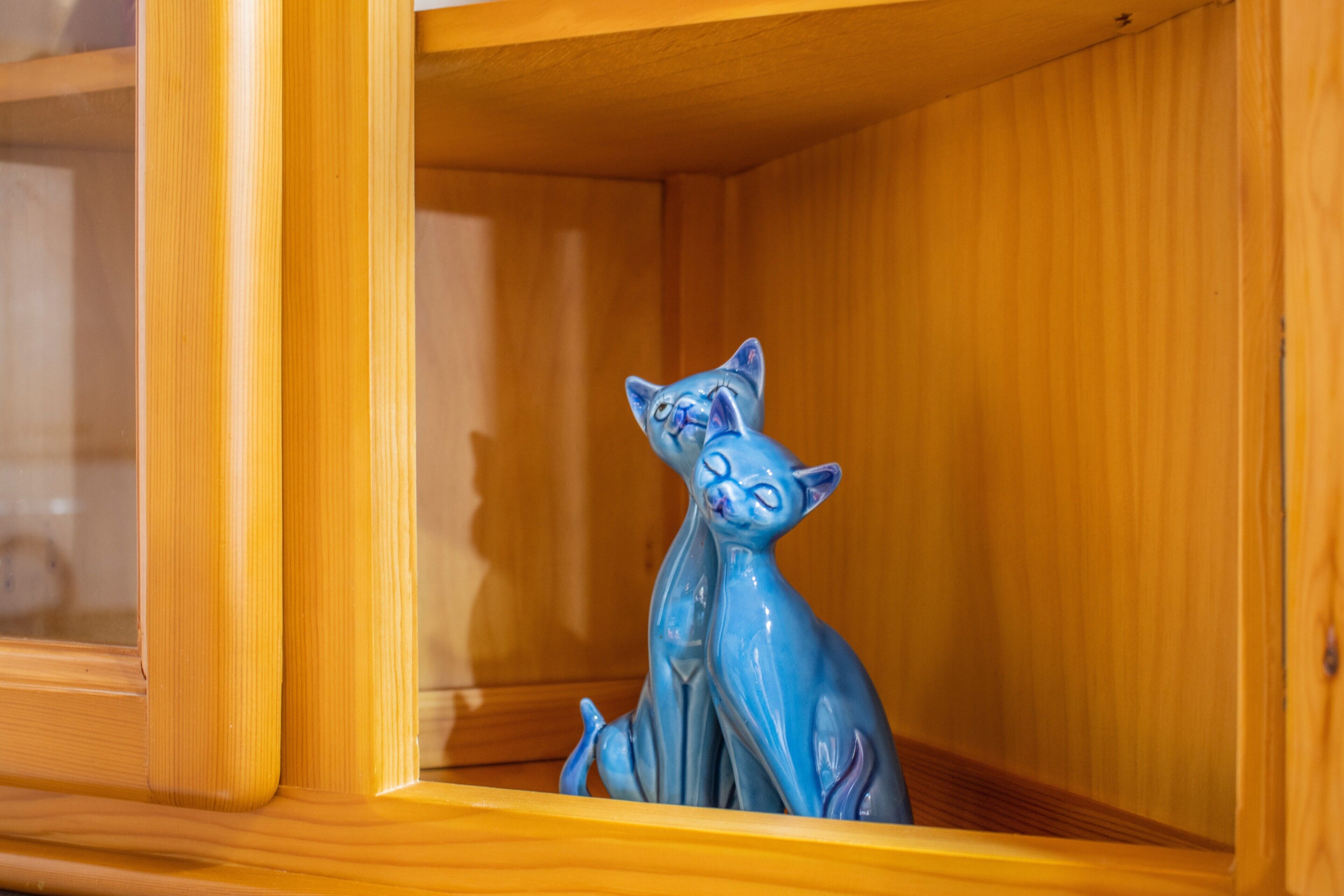 Uma estatueta de gato azul de cerâmica dentro de um armário de madeira.