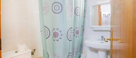 Un baño con cortina de ducha, inodoro, lavabo y espejo.