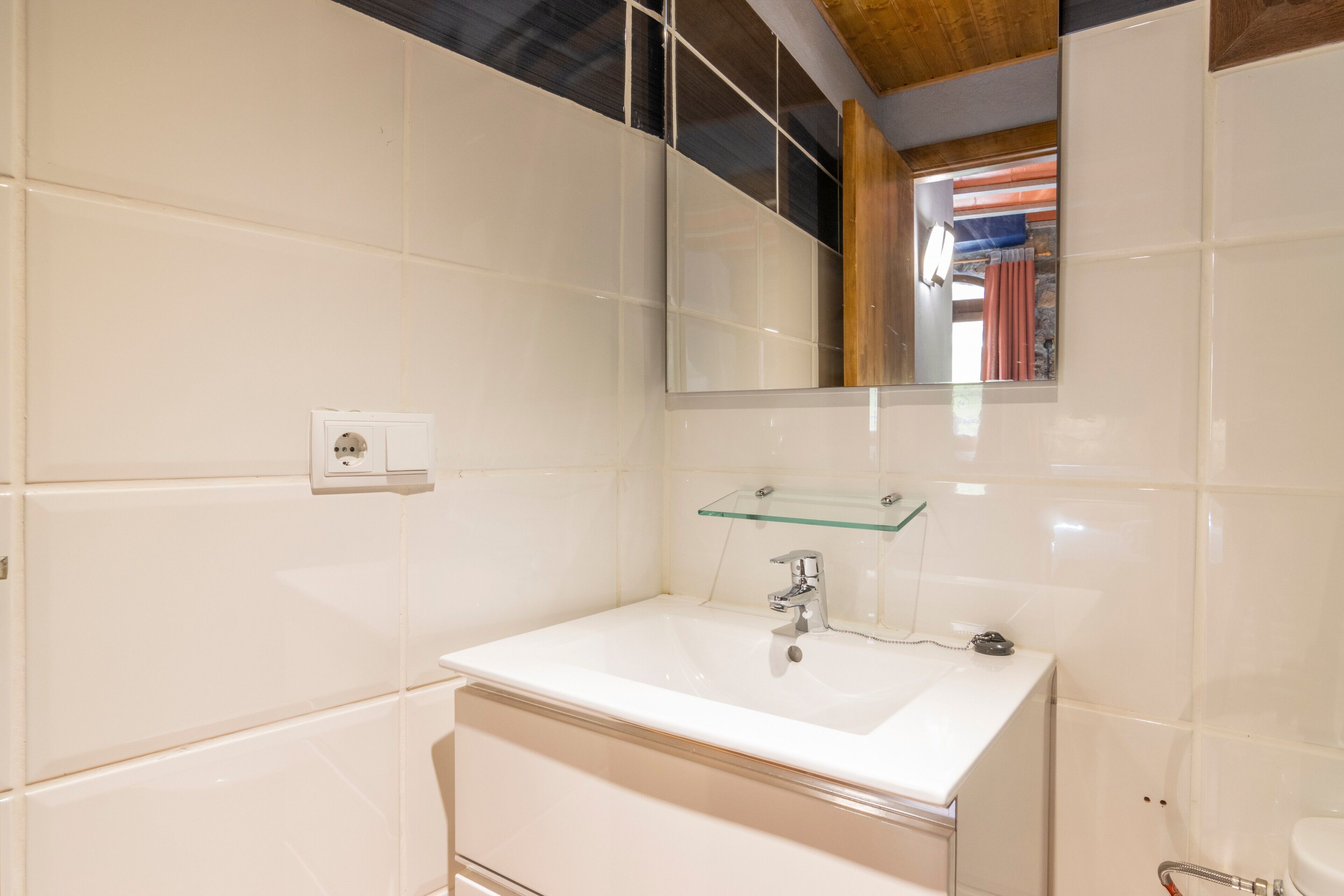 Een badkamer met een wit wastafelmeubel, een glazen plank, een spiegel en een handdoekhouder.