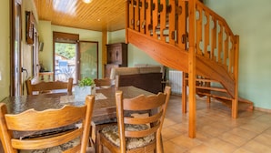 Un espace repas avec une table et des chaises en bois, un escalier et une vue sur l’extérieur.