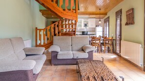 Un salon avec un escalier en bois, un canapé, une table basse en bois et, au fond, une cuisine.
