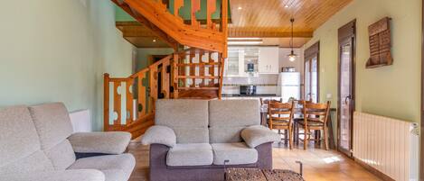 Una sala de estar con escalera de madera, un sofá, una mesa de centro de madera y una cocina al fondo.